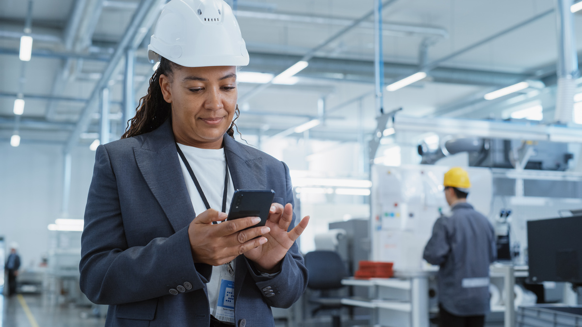 Industrial professional reviewing LinkedIn on a smartphone on a manufacturing floor.